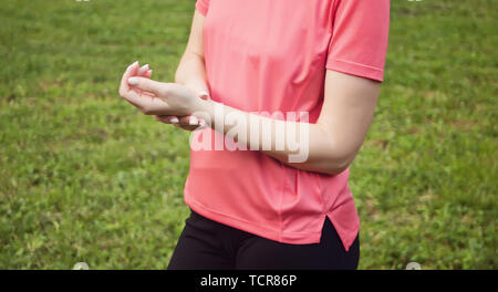 Medizin Gesundheit. Junge sportliche Frauen tragen rosa Training t-shirt Prüfung Puls am Handgelenk Nahaufnahme. Natur Hintergrund. Stockfoto