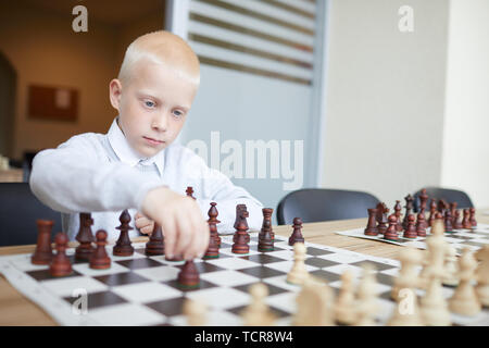 Blonde Schüler in weißem Hemd, erste Schach bewegen im Spiel mit imaginären Gegner Stockfoto