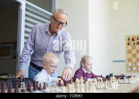 Im Alter von männlichen Lehrer mit Brille hilft beiden Schüler mit Schach lernen SCHACH Kombinationen während Klasse Stockfoto