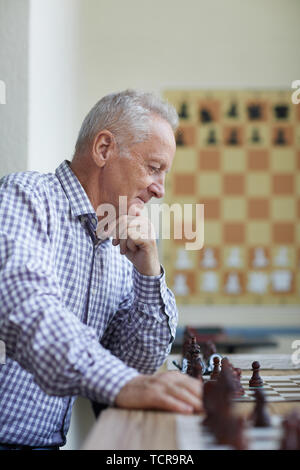 Alter Mann in kariertes Hemd mit silbernen Haar mit einem Lächeln am Schachbrett und Analyse interessante schach spiel Stockfoto