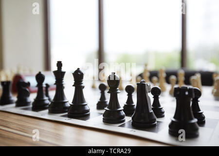Holz- Schachfiguren in perfekter Ordnung stehend am Tisch vor dem Fenster im Klassenzimmer der Chess Club angeordnet Stockfoto