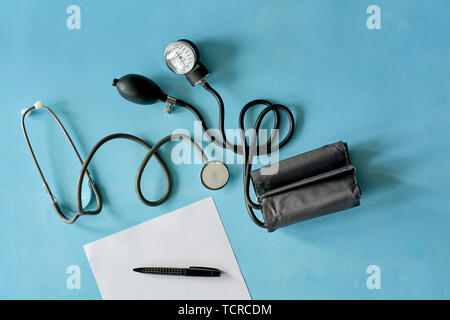 Weißes Blatt Papier mit schwarzer Tinte und phonendoscope Stethoskop, sphygmomanometer auf blauem Hintergrund. Stockfoto