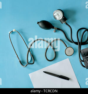 Weißes Blatt Papier mit schwarzer Tinte und phonendoscope Stethoskop, sphygmomanometer auf blauem Hintergrund. Stockfoto