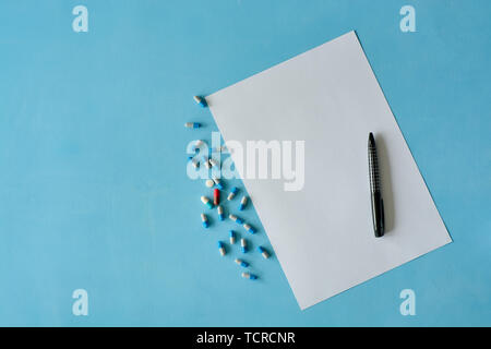Weißes Blatt Papier mit schwarzer Tinte und farbigen verschiedene Tabletten, Kapseln auf blauem Hintergrund. Stockfoto