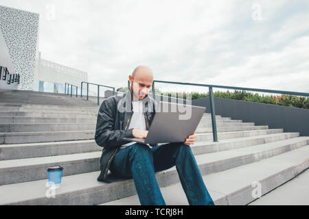 Attraktive nach erfolgreichen Kahlen bärtigen Mann in schwarzer Jacke mit Laptop Treppe im City Stockfoto