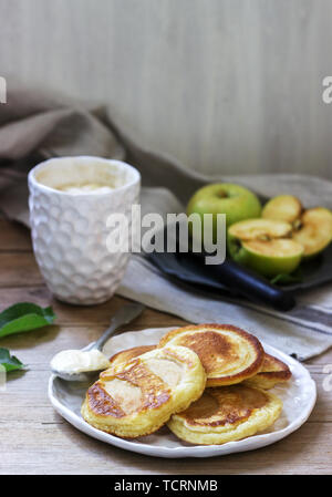 Hausgemachte apple Fritters mit saurer Sahne, Kaffee und grüne Äpfel auf einer hölzernen Hintergrund. Rustikaler Stil, selektiven Fokus. Stockfoto