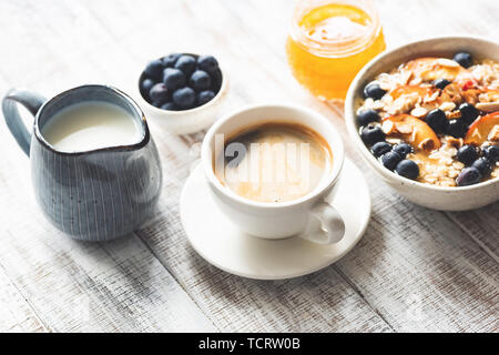 Tasse Kaffee Espresso und Frühstück Haferflocken Haferbrei mit Früchten, Beeren, Honig auf weiße Holztisch Hintergrund Stockfoto