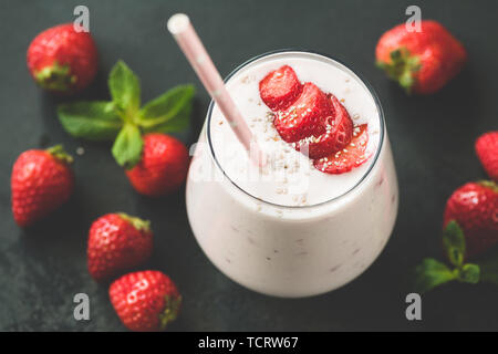 Erdbeer Milchshake oder Smoothie in Glas mit rosa Strohhalm auf schwarzem Hintergrund. Getonten Bild Stockfoto