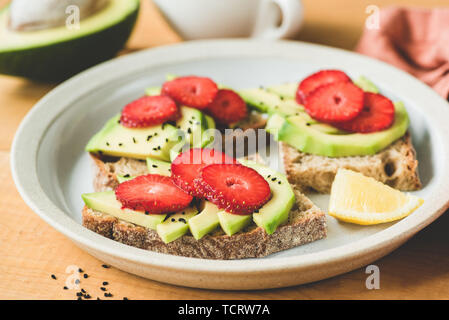 Roggen Toast mit Avocado und Erdbeere an der Platte. Gesund vegan vegetarische Kost Stockfoto