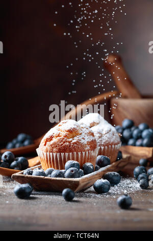 Muffins und Heidelbeeren bestreut mit Puderzucker auf einen alten Holztisch. Stockfoto