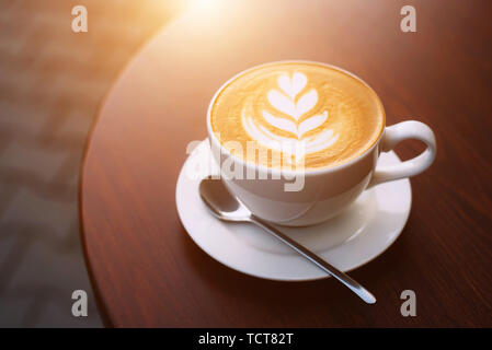 Frisch gebrühten Cappuccino in einer Tasse weiße Farbe auf einem hölzernen Tisch in den Morgen beim Frühstück Stockfoto