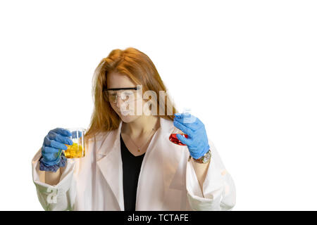 Ingwer behaarte Teen Girl in Laborkittel, Handschuhe und Schutzbrille holding Bechergläser von bunten Flüssigkeiten. Stockfoto