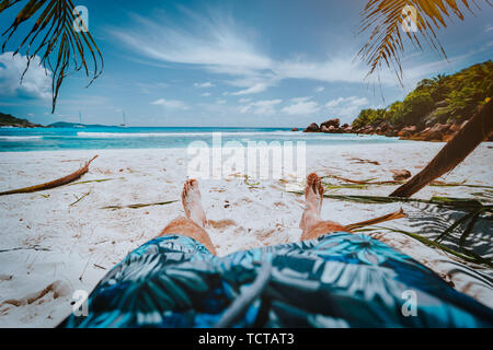 POV-shot von Mensch tragen blaue Badeshorts Festlegung auf einem schönen Sandstrand Cosos tropischen Strand Anse, La Digue, Seychellen Stockfoto