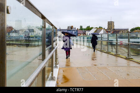 Shoreham-by-Sea, Sussex, UK. 10. Juni 2019. Sonnenschirme sind als Menschen die Adur Fußgängerbrücke über den Fluss Adur in Shoreham heute bei nassem Wetter Kreuz. Es wird prognostiziert, dass Teile der Osten und Südosten ein Monate Niederschlag in den nächsten Tagen in das, was als Monsun Juni genannt wird. Foto: Simon Dack/Alamy leben Nachrichten Stockfoto