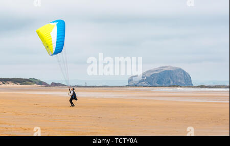 Tyninghame Strand, East Lothian, Schottland, Vereinigtes Königreich, 10. Juni 2019. UK Wetter: Nicht ganz genug Wind ein Gleitschirm mit einem Flügel Drachen in der Luft auf die Weite der Sandstrand bei Ebbe mit dem Bass Rock gannet Kolonie am Horizont erhalten Stockfoto