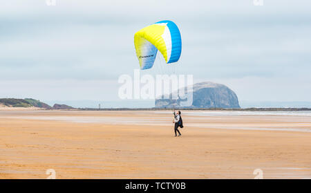 Tyninghame Strand, East Lothian, Schottland, Vereinigtes Königreich, 10. Juni 2019. UK Wetter: Nicht ganz genug Wind ein Gleitschirm mit einem Flügel Drachen in der Luft auf die Weite der Sandstrand bei Ebbe mit dem Bass Rock gannet Kolonie am Horizont erhalten Stockfoto