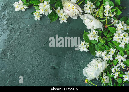 Jasmin und weiße Pfingstrose auf dunklem grün Betonoberfläche Tabelle. Ansicht von oben, flach, kopieren Sie Text. Schöne Grußkarte. Stockfoto