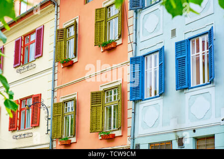 Bunte (Rot, Grün und Blau) Fensterläden aus Holz auf weißen Fenstern, in den hellen Tag. Drei Gebäude, die Seite an Seite in Sibiu, Rumänien. Stockfoto