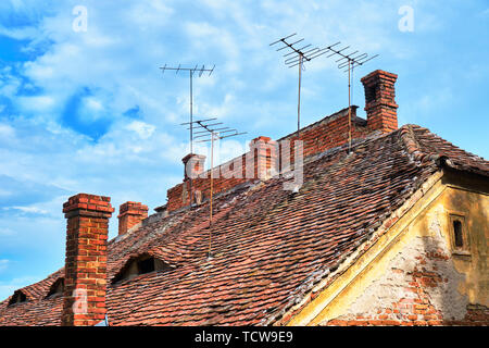 Traditionelle Dächer in Hermannstadt, Rumänien, mit Auge geformt Windows, gemauerte Schornsteine und alten TV-Antennen an der Spitze, an einem hellen Tag mit blauem Himmel und weißen Wolken Stockfoto