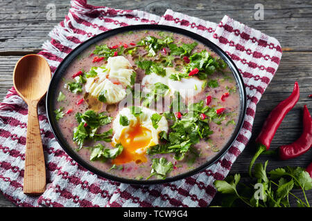 Hot mexikanische scharfe rote Kidney-bohnen-Suppe mit pochierten Eiern und Koriander in einem schwarzen Schüssel auf einem Holztisch, Ansicht von oben, close-up Stockfoto