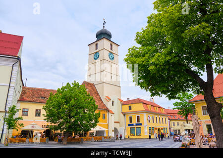 Sibiu, Rumänien - 27. Mai, 2019: Der Rat Turm (Turnul Sfatului) in Hermannstadt, von den wichtigsten großen Platz gesehen, mit grünen Bäumen, an bewölkten Tag. Bevölkerung Stockfoto