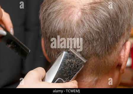 Frau Friseur schneidet die Haare des Mannes mit elektrischer Haarschneider Trimmer Stockfoto