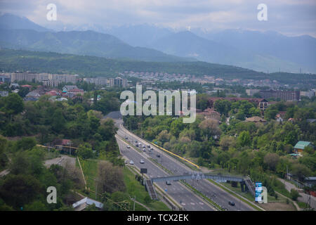 Panoramablick auf die Stadt Almaty, mit Straße, Industriegebiet, die Berge und den Himmel mit Wolken. Von Kok Tobe, Kasachstan gesehen. Stockfoto