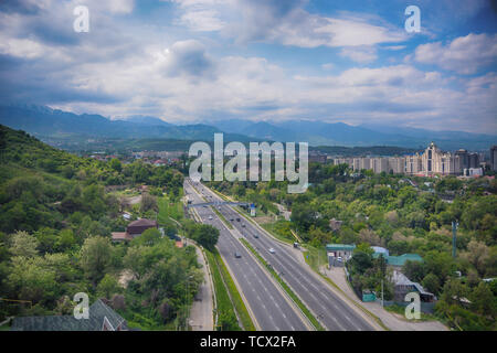 Panoramablick auf die Stadt Almaty, mit Straße, Industriegebiet, die Berge und den Himmel mit Wolken. Von Kok Tobe, Kasachstan gesehen. Stockfoto