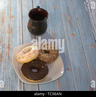 Eine Tasse Kaffee und Donuts in das Sahnehäubchen auf eine Platte liegen auf dem Tisch. Stockfoto