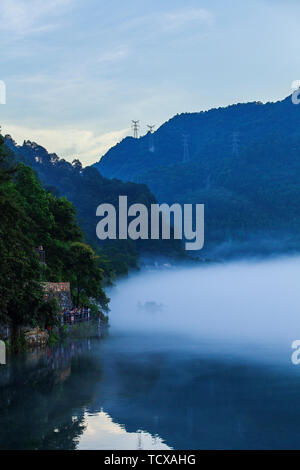 Der Nebel füllt Xiao Dongjiang 9 (Am frühen Morgen des Sommers, dicker Nebel durchdringt Xiao Dongjiang und in der Licht und Schatten auf den Sonnenaufgang, Fischer bereiten Sie Fisch.) Stockfoto