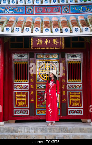 Eine junge Vietnamesin in einem traditionellen Ao Dai-Kleid und steht vor einem Tempel im historischen Stadtzentrum von Hoi an, Vietnam Stockfoto