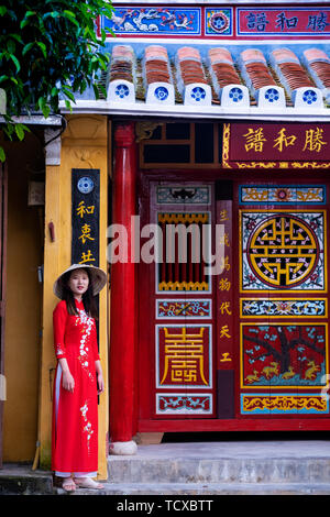 Eine junge Vietnamesin Tragen eines traditionellen Ao Dai Kleid und stehen vor einem Tempel im Herzen der historischen Altstadt, Hoi An, Vietnam, Indochina, Sou Stockfoto