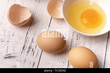 Frische Eier auf den Tisch, gebrochene Eier in eine Schüssel geben. Stockfoto