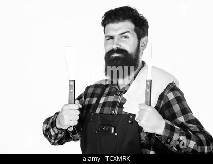 Besten Grill Kochgeschirr. Der bärtige Mann mit Grill Werkzeuge in den Händen. Grill kochen mit Spachtel und Grill Gabel. Happy hipster Holding Werkzeuge aus rostfreiem Stahl für die Vorbereitung der Grill essen. Stockfoto