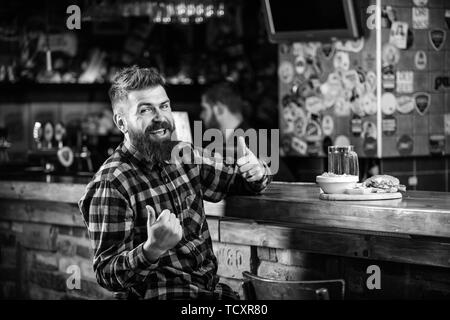 Kalorienreiche Snacks. Hipster entspannen im Pub. Pub ist ein entspannender Ort Drink zu entspannen. Brutale hipster bärtigen Mann an der Theke sitzen. Mann mit Bart Bier trinken essen burger Menü. Essen im Pub. Stockfoto