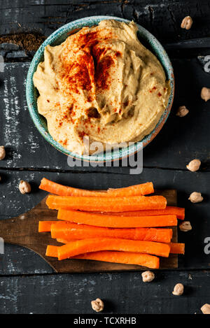 Hohe Betrachtungswinkel und einer hausgemachten Hummus gewürzt mit Paprika in einer grünen Keramik Teller serviert und einige Streifen von Karotte, in sie eintauchen, auf einem dunkelgrauen Rus Stockfoto