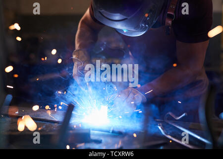 Konzentrierter Arbeiter in Schweißen Maske Schmelzen von Metall mit Schweißen Werkzeug Stücke zusammen, die in Workshop Stockfoto