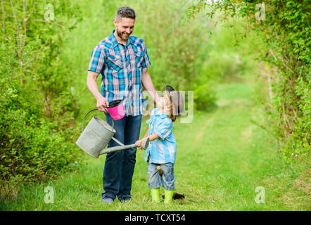 Eco Farm. mit Gießkanne und Topf. Gartengeräte. kleiner Junge Kind helfen Vater in der Landwirtschaft. Vater und Sohn in Cowboy Hut auf Ranch. happy Earth Day. Stammbaum nursering. Am besten in unserer Sphäre. Stockfoto