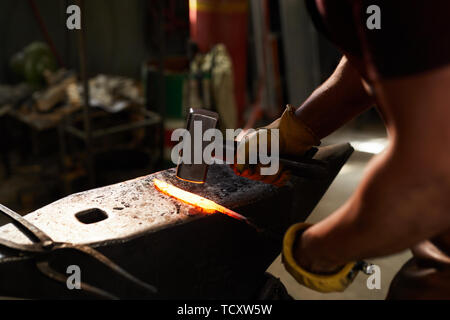 Nahaufnahme der unkenntlich Schmied an Stahl Amboss und Gestaltung beheizten Bar mit einem Hammer in der Werkstatt Stockfoto