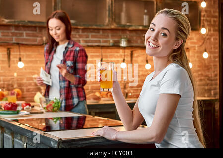 Portrait von blondes Mädchen tragen weiße T-Shirt, mit frischem Saft, mit Blick auf die Kamera und lächelnd. Ihr dunkelhaarigen Freund in kariertem Hemd ist Co Stockfoto