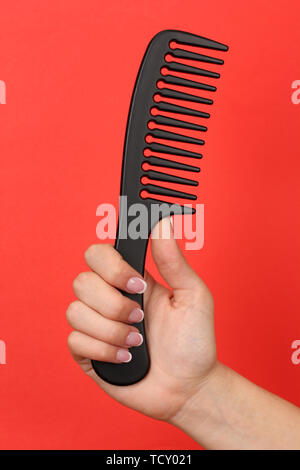 Schwarz Kamm in weiblicher Hand auf farbigen Hintergrund Stockfoto