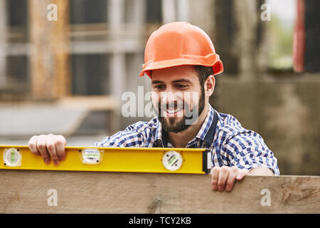 Genaue Messungen. Freundliche Bauarbeiter in gelbem Helm Kontrolle des ein Brett aus Holz und Bau arbeiten si Stockfoto