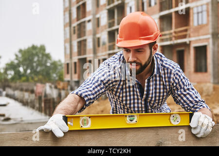 Genauigkeit und Qualität. Bauarbeiter in gelbem Kontrolle des ein Brett aus Holz während der Arbeit auf der Baustelle. Bau Stockfoto