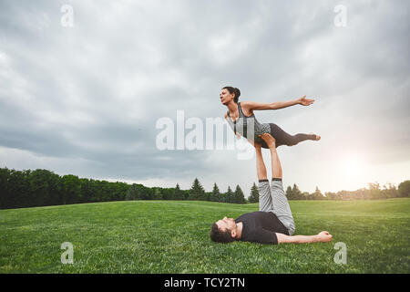 Gesunde Lebensweise. Starke Mann liegen auf Gras und Balancing Frau auf seine Füße. Junges Paar üben acro Yoga in der Natur. Gesunder Lebensstil Konzept. Stockfoto