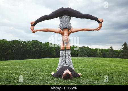 Wochenende Tätigkeiten. Sportlich schönes Paar Paar Yoga üben in der Natur. Mann lag auf einem Gras, Holding und Balancing Frau auf seine Beine. Acro yoga c Stockfoto