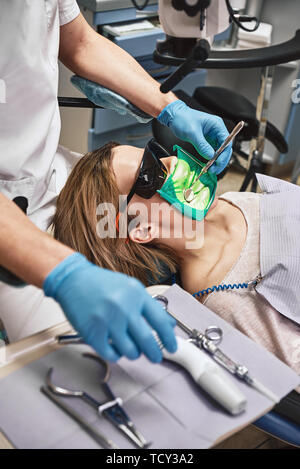 Portrait der weiblichen Patienten in Gläser mit geöffnetem Mund. Sie hat etwas modrig. Zahnarzt der Festsetzung mit zahnmedizinischer Werkzeuge. Behandlung. Moderne zahnmedizinische clin Stockfoto