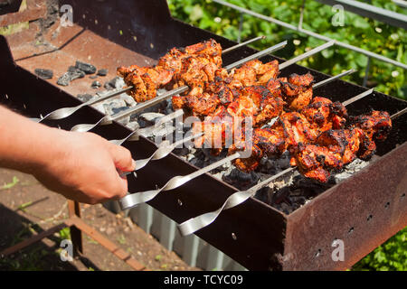 Auf dem Grill, eine Menge Fleisch gebraten am Spieß, der Koch dreht seine shish Kebabs. Hand eines Mannes, Pommes leckere Fleisch von Schwein am Spieß in Stockfoto