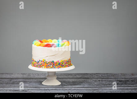 Geburtstag Kuchen mit Rainbow Vereisung und bunten Streuseln über einen grauen Hintergrund. Stockfoto
