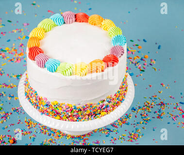 Geburtstag Kuchen mit Rainbow Vereisung und bunten Streuseln über einen blauen Hintergrund. Stockfoto