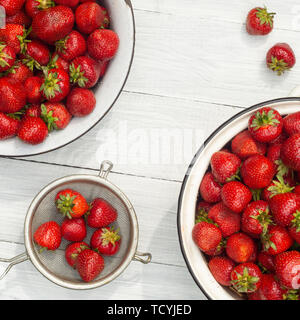 Erdbeeren in Metall Schalen und Sieb auf einem weißen Holztisch. Ansicht von oben Stockfoto